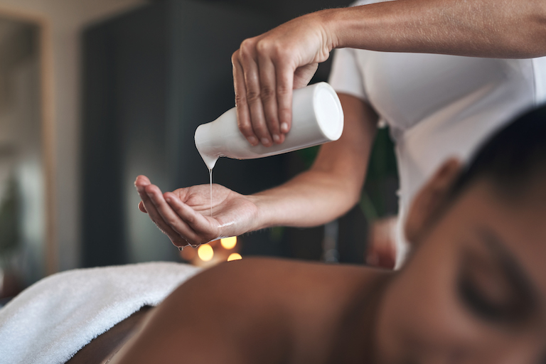 Closeup shot of a massage therapist pouring body oil into her hands while giving a massage to a customer at a spa